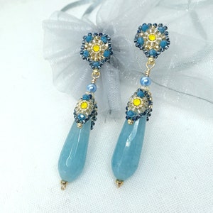 Può includere: Un paio di orecchini pendenti con fiori di perline blu e gialle e pietre blu acquamarina a forma di lacrima.