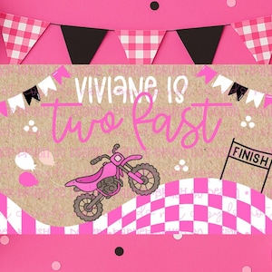 Pu&ograve; includere: Un banner per feste di compleanno rosa e bianco con la scritta "Viviane ha due anni veloce" e un'illustrazione di moto da cross rosa. Lo striscione &egrave; decorato con palloncini neri e rosa e bandiere a scacchi.