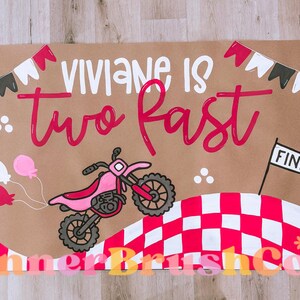 Pu&ograve; includere: Striscione marrone con la scritta "Viviane is two fast" in bianco e rosa. Lo striscione presenta una moto rosa, palloncini e un traguardo a scacchi. I gagliardetti decorativi sono in alto.