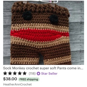 May include: Crocheted brown, tan, and red striped pants with a sock monkey face. The face has black eyes and a red mouth.