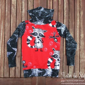 Könnte beinhalten: Ein langärmeliges Kinder-T-Shirt mit rotem Oberteil und einem Waschbär-Motiv. Die Ärmel und der Rollkragen sind schwarz mit einem weißen Kritzelmuster. Das Shirt hat ein tailliertes Design und ist aus einem weichen Material gefertigt.