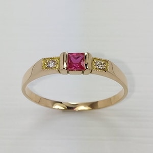 May include: A gold ring with a pink square gemstone and two smaller white gemstones.