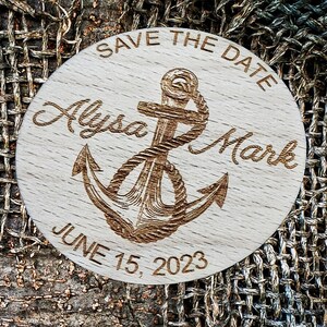 May include: A round wooden save the date sign with a nautical theme. It features a carved anchor with rope, the text "Save the Date", the names "Alyssa Mark", and the date "June 15, 2023".