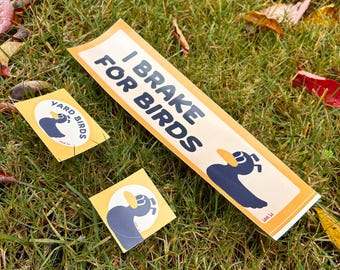 May include: Three stickers and a long sign with the text "I Brake for Birds" and a cartoon duck. The stickers say "Yard Birds" and feature the same duck graphic. All items are on a bed of green grass.