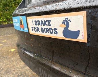 May include: Two bumper stickers are affixed to a black car. The first sticker has a cartoon image of a duck and the text "I BRAKE FOR BIRDS". The second sticker has a cartoon image of a person and the text "STINKY TAILGATE".