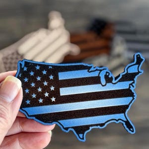 Peut inclure: Une silhouette bleue et noire des États-Unis d'Amérique avec un design de drapeau américain à fine ligne bleue.