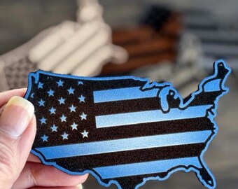 May include: A blue and black outline of the United States of America with a thin blue line American flag design.