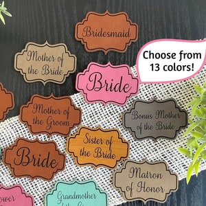 May include: Assortment of 13 different colors of leather wedding party labels with various titles including Bride, Bridesmaid, Maid of Honor, Mother of the Bride, Mother of the Groom, Sister of the Bride, Matron of Honor, Flower Girl, Grandmother of the Bride, and Grandmother of the Groom.