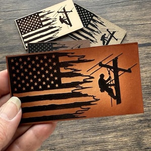 May include: Three leather patches with an American flag and a silhouette of a lineman working on a power line. The patches are brown, tan, and black.