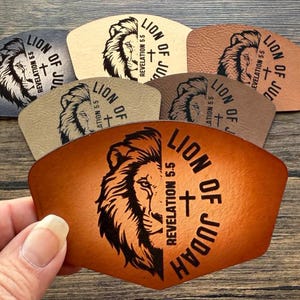 May include: A selection of leather patches in various colours, each displaying a lion's head and the text "LION OF JUDAH REVELATION 5.5". The patches are in shades of brown, tan, and grey, with a black graphic design.
