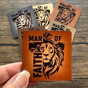 May include: A collection of square leather patches in various colors, each featuring a lion's head and the words "MAN OF FAITH." The patches are in shades of brown, gray, and beige, with the lion and text in a contrasting color.