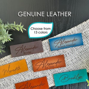 May include: A collection of personalized leather name tags in various colors, including brown, orange, blue, and teal. The tags feature different names and titles, such as "Alexander", "Meredith", and "Brooklyn". The text "Genuine Leather" and "Choose from 13 colors" is also visible.