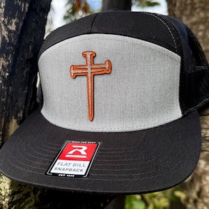 Puede incluir: Gorra snapback de visera plana negra y gris con parte trasera de malla. La gorra presenta un panel frontal gris con un diseño de cruz naranja. También son visibles una visera negra y una etiqueta que dice "FLAT BILL SNAPBACK".