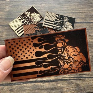 May include: A brown leather patch with a firefighter in a helmet and a US flag with flames behind them.