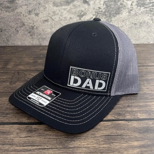 May include: Black and gray trucker hat with a white embroidered patch that says "BONUS DAD".