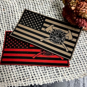May include: Two American flag patches with a firefighter emblem. The top patch is brown with black stars and the bottom patch is black with red stripes and stars. Both patches have a crossed axe design with a firefighter helmet and the words "Fire Dept."