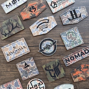 May include: A collection of 14 camouflage patterned patches with various business names and logos. The patches are in a variety of shapes and sizes, including squares, circles, and rectangles. The patches are all made of a durable material and have a high-quality finish.
