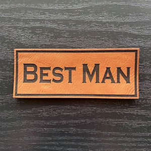 May include: A brown leather patch with black stitching and the text "BEST MAN" in black lettering.