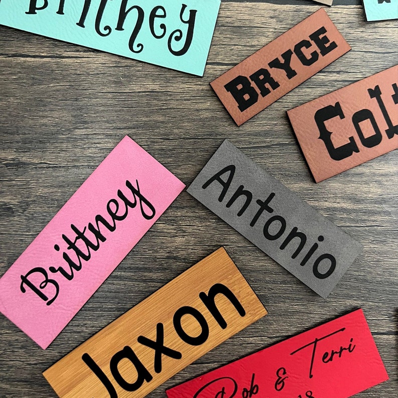 May include: A collection of personalized name tags in various colors and materials. The names include "Britney", "Jaxon", "Antonio", "Bryce", "Colt", and "Terri".