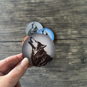 May include: A set of four round coasters featuring a black and white wolf howling at the moon. The coasters are made of leather and have a distressed look.