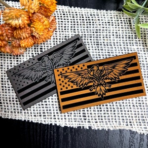 May include: Two wooden plaques with an American flag design and an eagle silhouette. One plaque is black with a gray eagle, and the other is brown with a gold eagle.