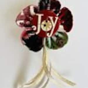 Könnte beinhalten: Handgefertigte Blumenbrosche mit rot-schwarzem Blütenblattdesign und dem Wort "JOY". Die Brosche hat goldfarbene Akzente und eine stielartige Basis, ideal, um jedem Outfit einen Hauch von Kunst zu verleihen.