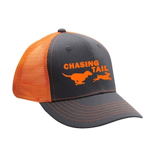 May include: A gray and orange trucker hat with the words "CHASING TAIL" and a dog chasing a rabbit in orange. The hat has a curved brim and an adjustable snapback closure.
