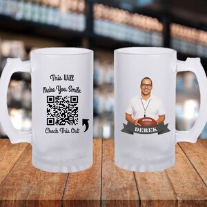 May include: Frosted glass beer mug with a white handle. One side features the text "This Will Make You Smile", a QR code, and "Check This Out". The other side displays a man holding a football, with the name "Derek" on a banner.