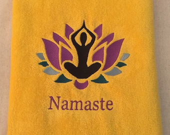 May include: Yellow towel with an embroidered purple lotus flower and a black silhouette of a person in a yoga pose. The text "Namaste" is embroidered below the image.