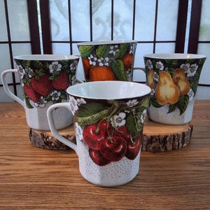 May include: A set of four ceramic mugs, each adorned with a different fruit illustration: strawberries, oranges, cherries, and pears. The mugs have white handles and are decorated with white flowers and green leaves.