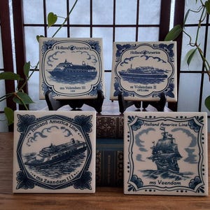 May include: Four square ceramic tiles with blue and white illustrations of Holland America Line ships. Each tile displays a different ship design and text, including "ms Volendam III 1999", "ss Volendam II 1972-1984", "ms Zaandam 111", and "ms Veendam".