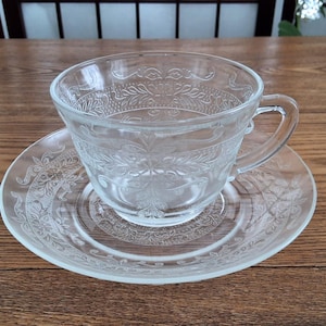 Peut inclure: Service à thé en verre transparent composé d'une tasse et d'une soucoupe. La tasse, avec anse, repose sur une soucoupe assortie. Les deux pièces présentent un motif floral et de feuilles en relief. Idéal pour le thé.