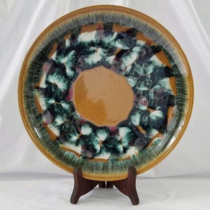 May include: A large, round ceramic plate with a brown glaze and a green and white design. The plate is on a wooden stand.