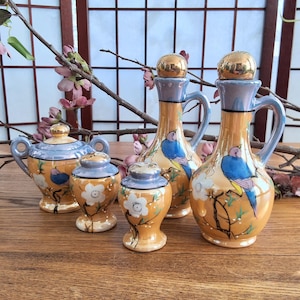 May include: A set of five vintage ceramic salt and pepper shakers and oil and vinegar bottles. The shakers and bottles are decorated with a floral design and blue birds. The bottles have gold lids.