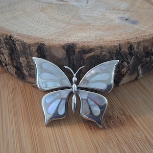 Peut inclure: Une broche en forme de papillon en argent avec des ailes en nacre. Les ailes sont d'un blanc irisé clair avec un contour argenté.
