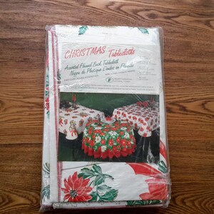 Peut inclure: Un paquet de nappes de table de Noël avec un motif de poinsettia rouge et vert. Le paquet comprend trois nappes : une ronde et deux rectangulaires. Le texte sur l'emballage indique "CHRISTMAS Tablecloths Assorted Flannel Back Tablecloths Nappe de Plastique L'endos en Flanelle".