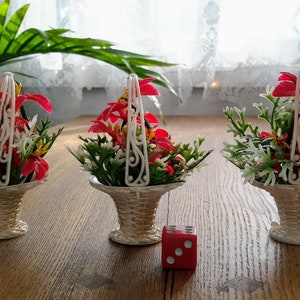 Peut inclure: Trois petits paniers en osier blanc avec des fleurs artificielles rouges et blanches. Les paniers ont des poignées en fil de fer blanc et sont posés sur une table en bois.