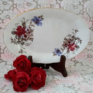 Peut inclure: Plat de service ovale blanc avec un bord doré et un motif floral composé de fleurs rouges, bleues et brunes.