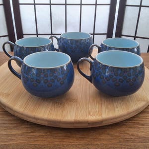 May include: Set of five blue and white ceramic soup bowls with a floral pattern. The bowls have a rounded shape and a handle on one side.