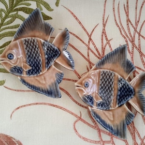 May include: Two ceramic fish wall decor pieces in brown and blue with a textured finish. The fish are stylized and have a 3D effect.