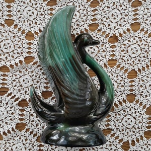 Peut inclure: Un vase en céramique en forme de cygne, de couleur noire et verte, avec un design stylisé. Le vase est en forme de cygne avec les ailes déployées.