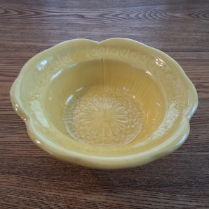 Peut inclure: Un bol en céramique jaune avec un bord festonné et un motif floral sur la base. Le bol a une finition brillante et est posé sur une surface en bois. Idéal pour servir ou décorer.