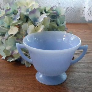 Peut inclure: Un bol à sucre en verre bleu clair avec deux anses. Le bol a un pied et est fait de verre opaque.