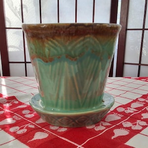 Peut inclure: Un pot en céramique vert glacé avec un bord brun et une soucoupe assortie. Le pot a un motif géométrique et un aspect vintage.