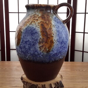 Peut inclure: Un grand vase en céramique brun et bleu avec une surface texturée et une poignée. Le vase a un glaçage marbré avec des couleurs brunes, bleues et blanches.