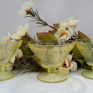 Peut inclure: Trois coupelles à dessert en verre jaune avec un motif floral délicat. Les coupelles ont un pied et sont parfaites pour servir de la glace, du pudding ou d'autres desserts.