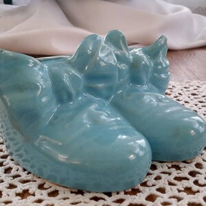 May include: A pair of blue ceramic shoes shaped like a planter. The shoes are glazed and have a shiny finish.