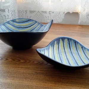 May include: Two ceramic bowls with a blue and yellow striped pattern. The bowls are on a wooden surface.