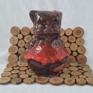 May include: A brown ceramic piggy bank with a red glaze, standing on a wooden coaster made of wood slices.