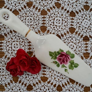 Peut inclure: Un serveur à gâteau en porcelaine blanche avec une bordure dorée et un motif de rose rose. Le serveur a une poignée en boucle.